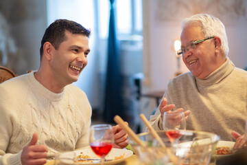 Fototapeta na wymiar Happy mid adult man talking to senior man at family dinner. Man and his father sitting at table and having conversation. Family dinner concept