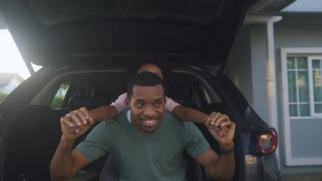 Happy African American father and little son have fun sitting in car trunk on a sunset day outside their home. Concept of weekend with family.