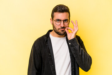 Young caucasian man isolated on yellow background with fingers on lips keeping a secret.