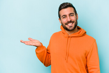 Young caucasian man isolated on blue background showing a copy space on a palm and holding another...
