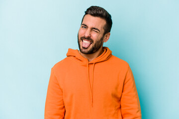 Young caucasian man isolated on blue background funny and friendly sticking out tongue.