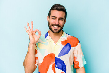 Young caucasian man isolated on blue background cheerful and confident showing ok gesture.