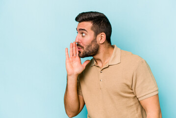 Young caucasian man isolated on blue background is saying a secret hot braking news and looking...