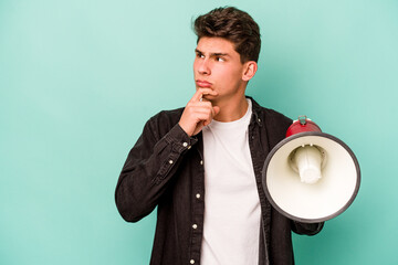 Young caucasian man holding a megaphone isolated on white background looking sideways with doubtful and skeptical expression.