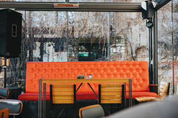 Interior of a cafe with an orange couch and glass walls surrounded by trees on a winter day
