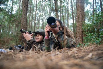 Focused mother and son taking pictures in forest. Family with modern cameras lying on ground, using camera and binoculars. Parenting, family, leisure concept