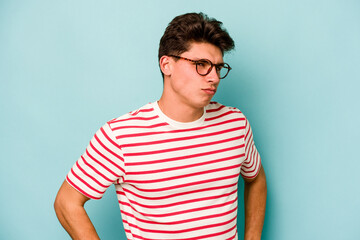 Young caucasian man isolated on blue background frowning face in displeasure, keeps arms folded.