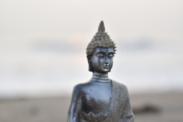 Closeup of the Buddha metallic idol profile on a sandy beach with the blurred background of the sea