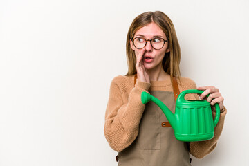 Young gardener woman holding a sprinkler isolated on white background is saying a secret hot braking news and looking aside