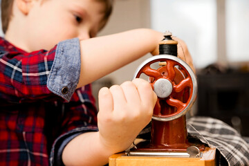 Learning professions. Boy sewing clothes with a mechanical hand sewing machine. Retro toy, reduced copy of original. Activities at home. Artistic mimic of real professional.