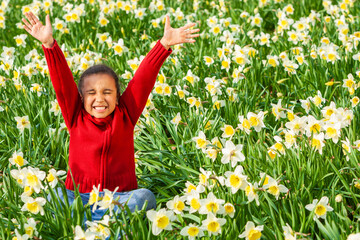 Naklejka na ściany i meble African American mixed race girl sitting arms raised celebrating in a field of daffodils