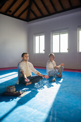 Two concentrated men meditating together. Focused middle adult men sitting in lotus pose with closed eyes. Hobby, spirituality, health concept