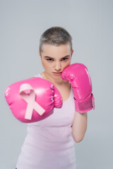 woman with breast cancer awareness ribbon on pink boxing glove standing in fight position isolated...