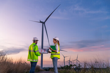 Fototapeta na wymiar Engineer wearing uniform ,helmet hold document inspection work in wind turbine farms rotation to generate electricity energy. Green ecological power energy generation wind sustainable energy concept.