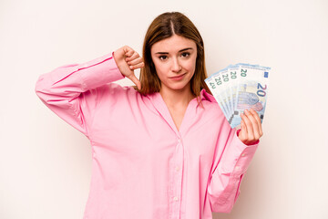 Young woman holding banknotes isolated on white background showing a dislike gesture, thumbs down. Disagreement concept.