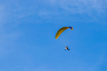 Paragliding flight with engine under blue sky.