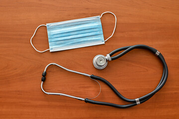 Top view of medical stethoscope and a protective face mask on a wood background. Disease prevention concept.