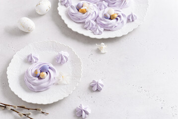 Mini Easter meringue nests with candy eggs on white plate on light background. Festive dessert....
