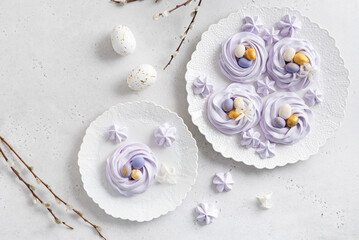 Mini Easter meringue nests with candy eggs on white plate on light background. Festive dessert. Confectionery, bakery, recipe concept. Top view, copy space