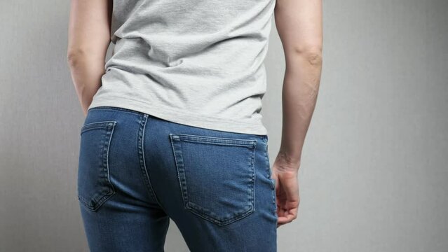 unrecognizable man twists booty standing against grey wall, close up