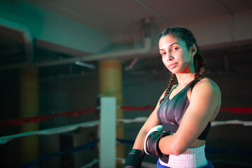 Close-up of beautiful boxer girl standing on ring. Thoughtful girl in sportswear and gloves posing after training boxing, calmly standing looking at camera. Female boxing and healthy lifestyle concept
