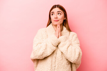 Young caucasian woman isolated on pink background praying, showing devotion, religious person looking for divine inspiration.
