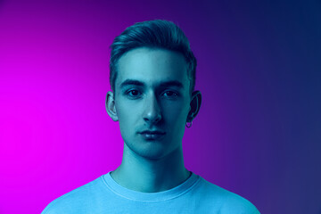 Portrait of young hansome man in white T-shirt lookig at camera, posing isolated over gradient pink purple background in blue neon light