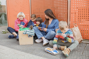 Family of Ukrainian refugee, senior woman and mother with three kids sit near charity center to get...