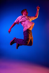 Fototapeta na wymiar Full-length portrait of young man in casual cloth jumping, posing isolated over blue background in pink neon light