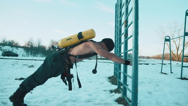 Bodybuilder with a naked torso doing push-ups from the bar in the cold with a drager on his back and pumping the latissimus dorsi