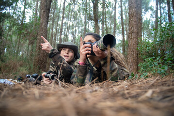 Merry mother and son taking pictures in forest. Family with modern cameras lying on ground, using...