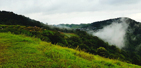 Obraz premium Beautiful range of green mountain, white cloud, small village and mist in the morning with copy space. Landscape view of hill at Phetchabun, Thailand. Natural wallpaper and Famous place for travel.