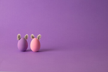 Row of colorful Easter eggs with willow bud ears painted in simple colors on a light purple background - side view with copy space