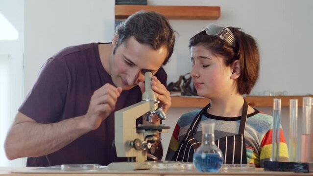A father helps his son Teenager in a research home laboratory to examine through a microscope against the background of laboratory equipment