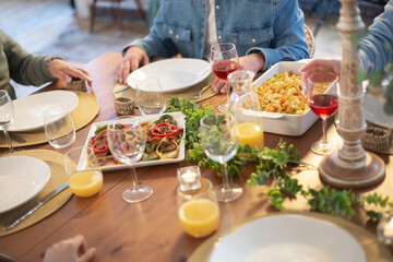 Family sitting at table having dinner together. Wooden table with salad, pasta and juice decorated with verdure. Family party concept