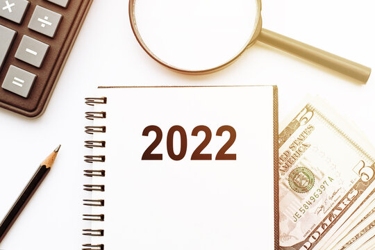 2022 New Year numbers in white note pad with magnifier, calculator, money and pencil on the office desk - Powered by Adobe