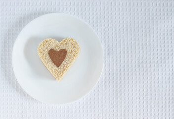 Top view of a heart-shaped cake sprinkled with cocoa lying on a white plate over a white tablecloth background