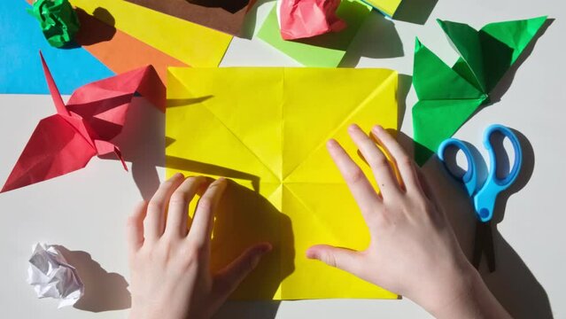 Children's hands do origami from colored paper on white background. Origami paper. DIY. Various school supplies. Concept of children's creativity, back to school.
