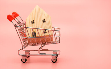 Miniature decorative wooden house in a shopping cart trolley isolated on pastel pink background...