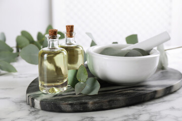 Fototapeta na wymiar Bottles of eucalyptus essential oil and plant branches on white marble table