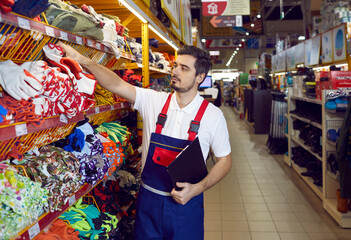 Salesman in uniform work in building hypermarket check products on shelves. Male consultant or assistant work restock goods in household or construction store. Shop assistance and consult.