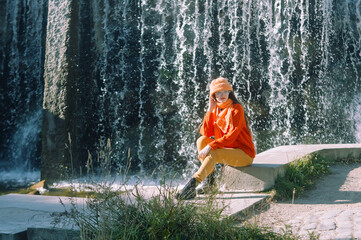 autumn portrait of a girl in a hat and orange sweater. woman sitting on the river bank.
