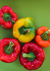 yellow, orange and red peppers on a green background, top view, texture of colorful vegetables, vertical format