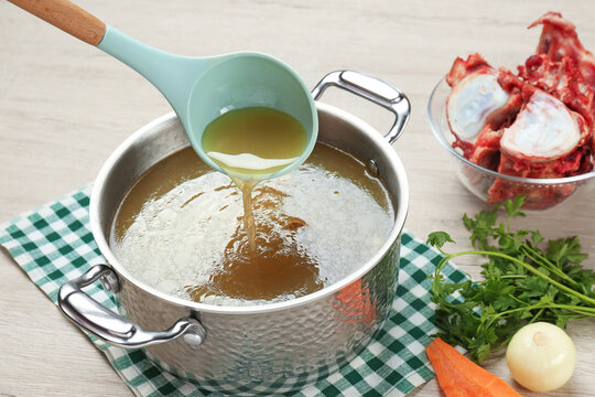 Delicious homemade bone broth and ingredients on wooden table