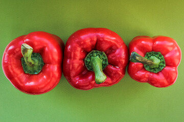 Three red peppers stand in a row on a green background, top view