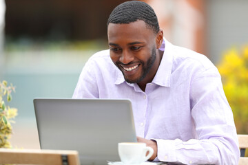 Happy man with black skin checking laptop content in a bar