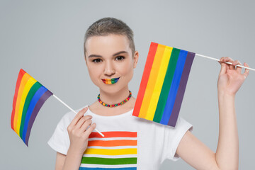 pretty woman with rainbow colors lips holding small lgbt flags isolated on grey.