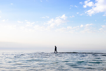 Obraz premium man wearing a long jacket walking on the water during a sunrise, Wet businessman walking to the water