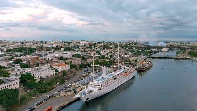 MSY Wind Surf ship anchored in Colonial zone port at sunset with cityscape. Aerial forward