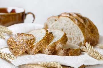 Freshly baked bread with ears of wheat on wooden board on white table, selective focus.